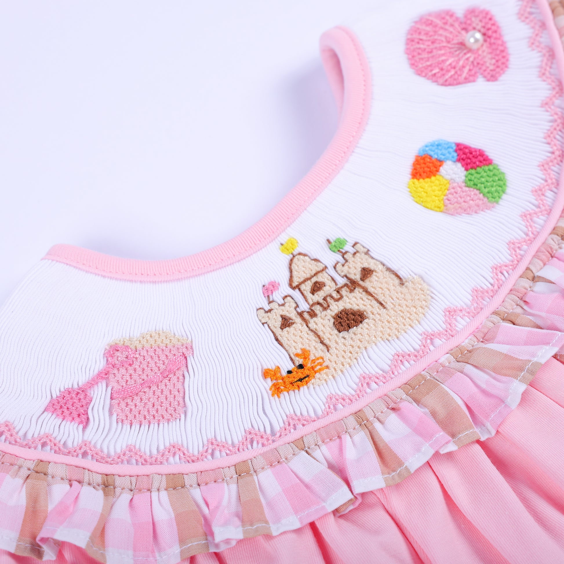 Extreme close-up of hand-embroidered sandcastle, beach ball, and shell motifs on a smocked baby bubble collar.