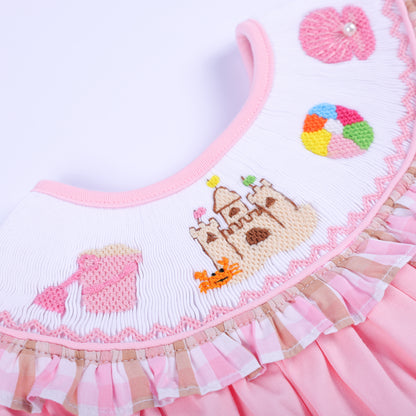 Extreme close-up of hand-embroidered sandcastle, beach ball, and shell motifs on a smocked baby bubble collar.