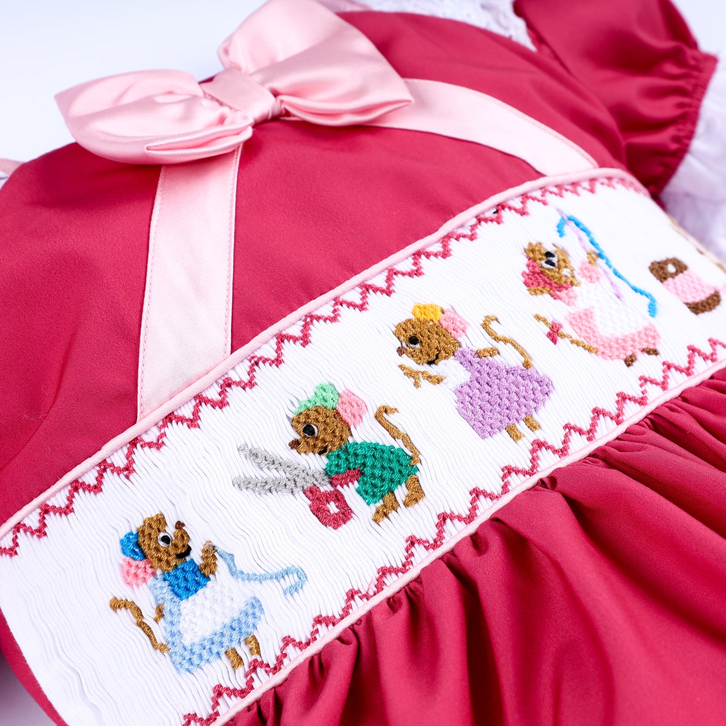 Close up of hand embroidered sewing mice scene on white smocked plate of pink hand smocked girls dress.