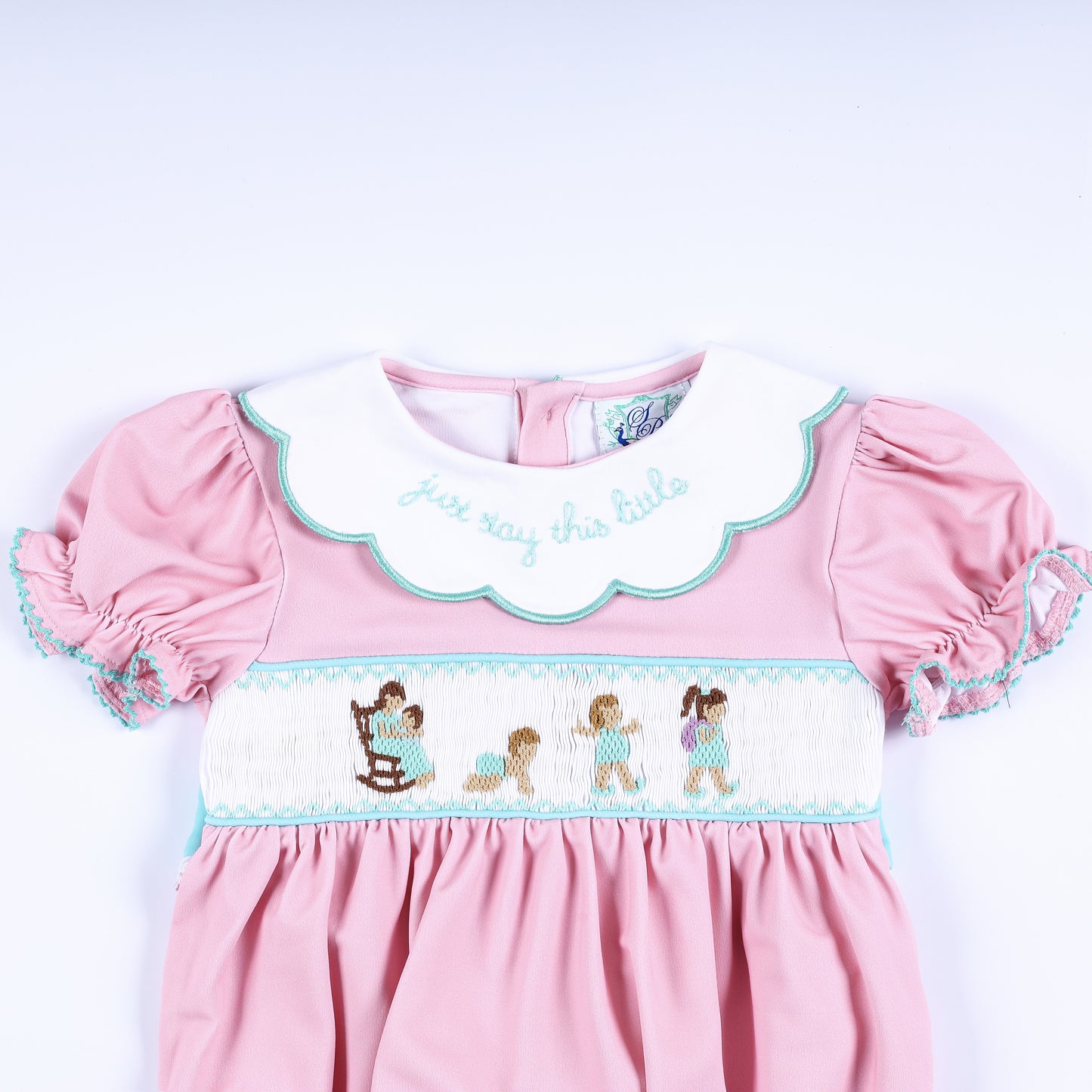 Upper front detail of hand smocked pink bubble showing embroidered collar quote and baby milestone smocking design.
