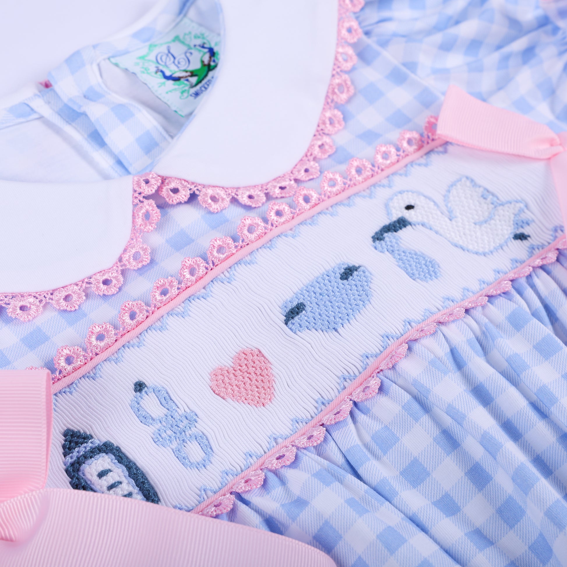 Detailed view of the hand-smocked chest panel featuring embroidered storks and baby motifs on a blue baby romper.
