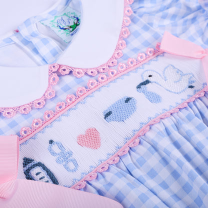 Detailed view of the hand-smocked chest panel featuring embroidered storks and baby motifs on a blue baby romper.