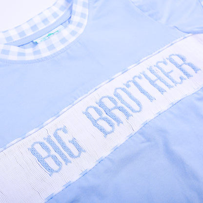 Angled close-up of delicate hand smocked and embroidered Big Brother lettering on light blue cotton shirt.
