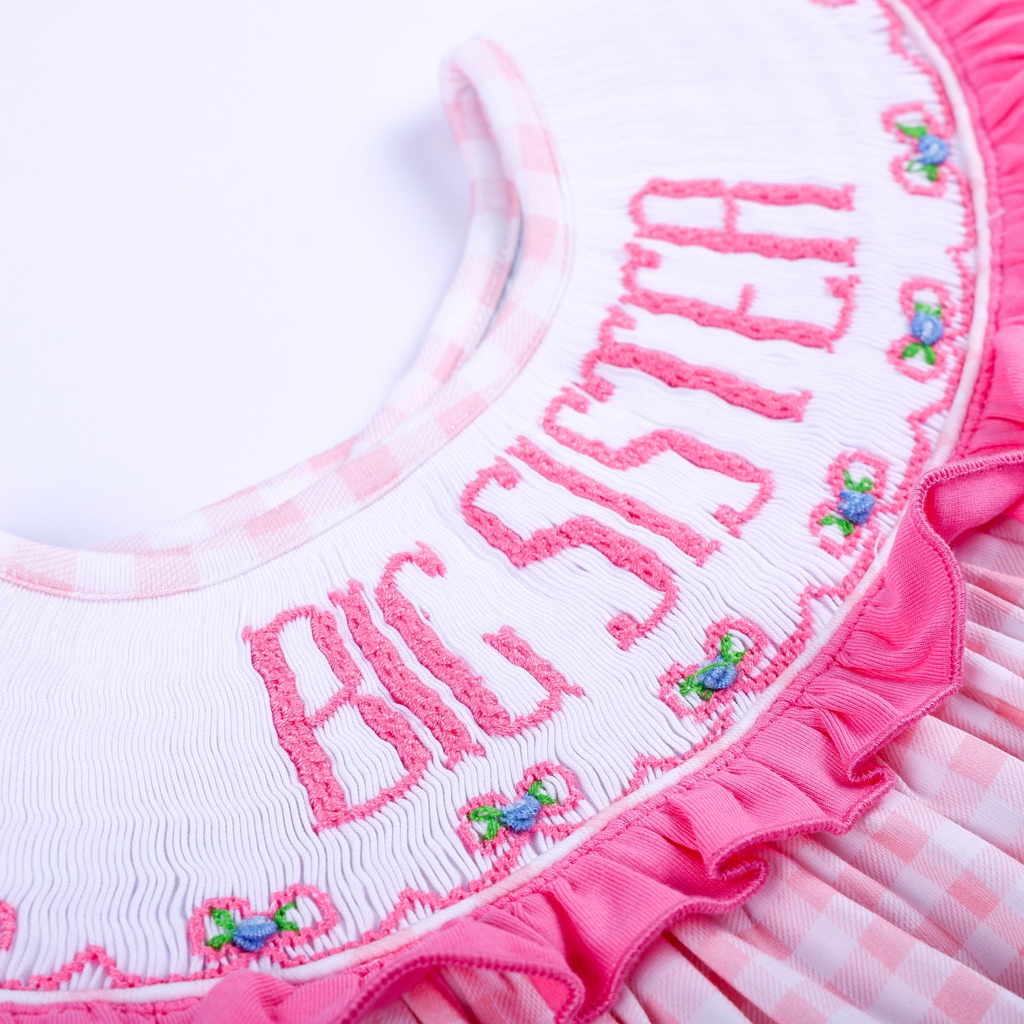 Macro view of delicate hand embroidered Big Sister text and tiny flowers on smocked pink ruffle collar.