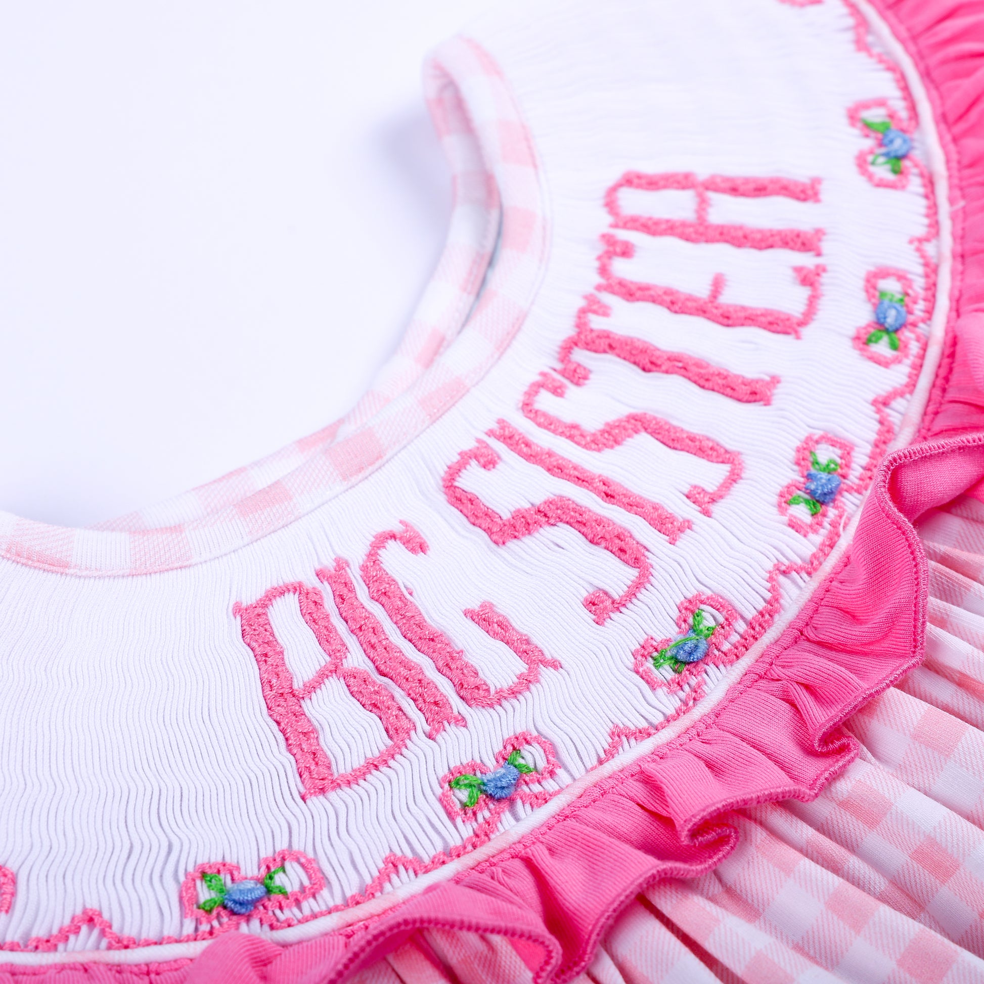 Macro view of delicate hand embroidered Big Sister text and tiny flowers on smocked pink ruffle collar.