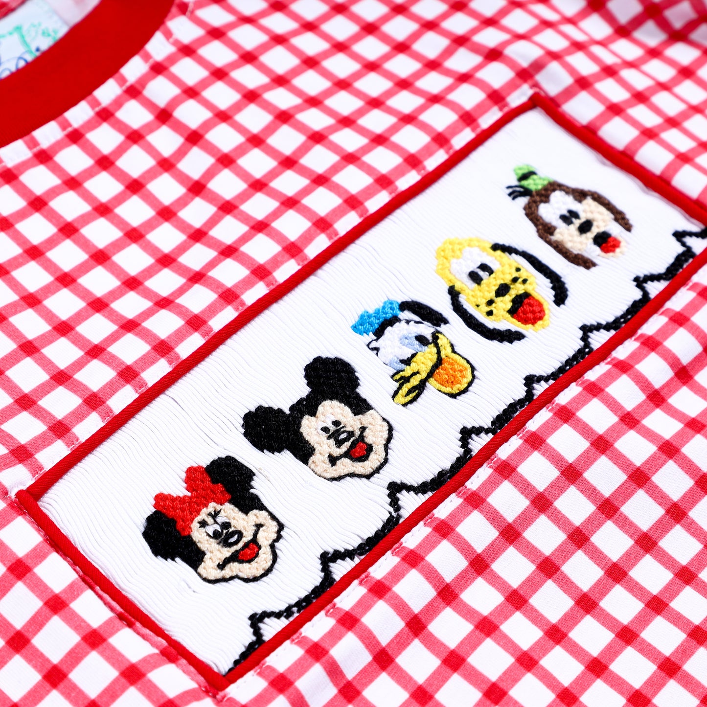 Detailed shot of hand embroidered fabulous 5 character faces on white smocking plate of red gingham boys shirt.