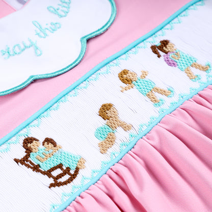 Close-up of intricate hand smocked panel with hand embroidered baby growth milestones on pink girl romper.