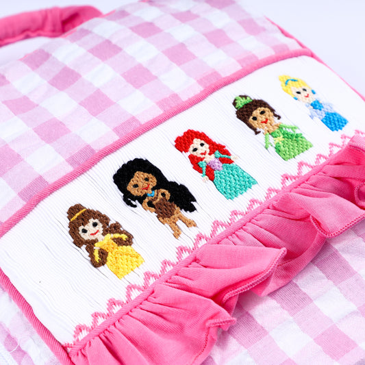 Close-up of hand-embroidered inclusive fairytale princesses on a smocked pink gingham ruffle lunch bag.