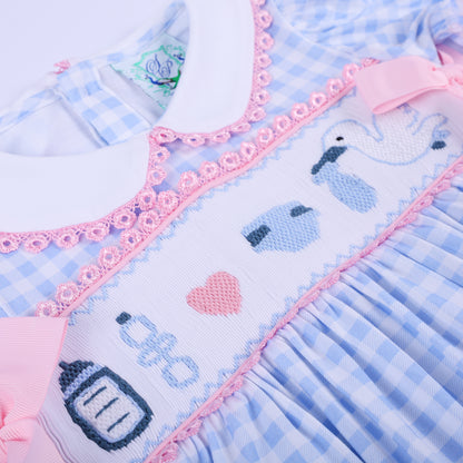 Angled view of hand smocked chest embroidery featuring baby bottle, rattle, heart, and diaper on gender reveal dress.