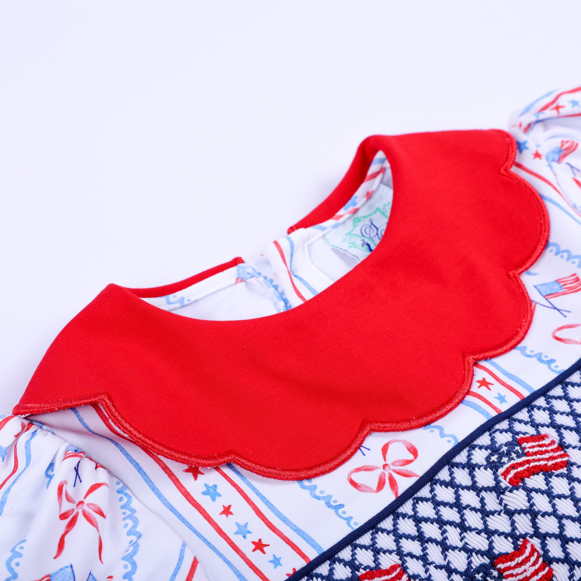 Close-up of red scalloped collar on America the Beautiful hand embroidered patriotic smocked baby bubble romper.
