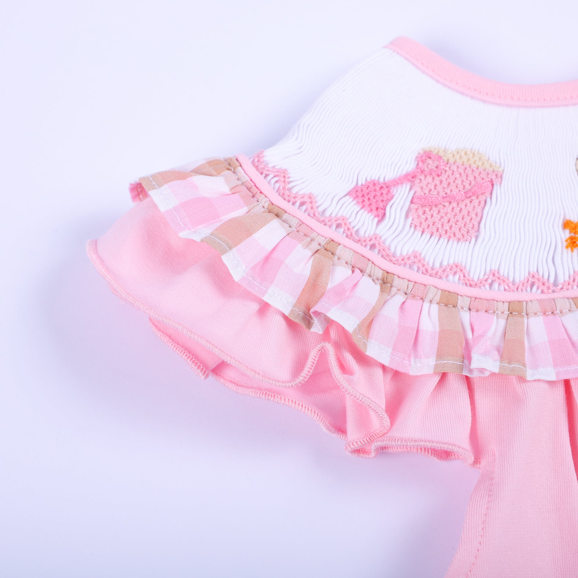 Close-up of pink flutter sleeve ruffle trim with gingham plaid accents on a hand-smocked beach baby bubble.
