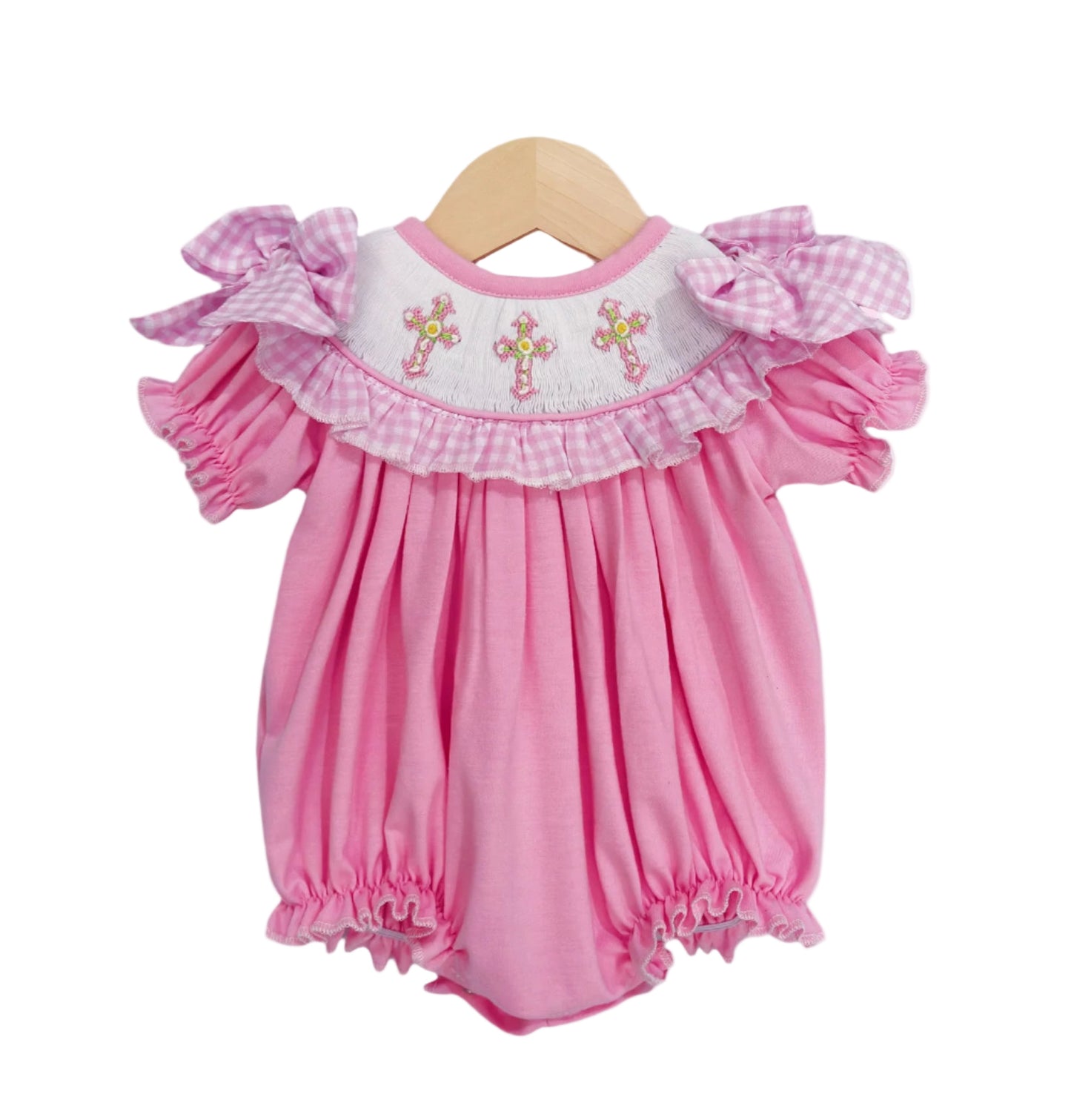 Hand-smocked pink baby girl bubble romper featuring embroidered cross yoke, gingham ruffle trim, and shoulder bows.