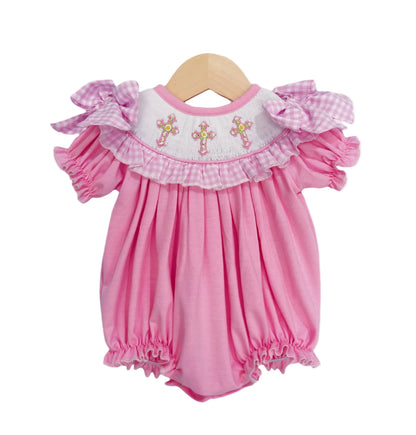 Hand-smocked pink baby girl bubble romper featuring embroidered cross yoke, gingham ruffle trim, and shoulder bows.