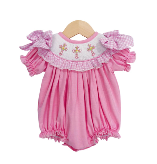 Hand-smocked pink baby girl bubble romper featuring embroidered cross yoke, gingham ruffle trim, and shoulder bows.