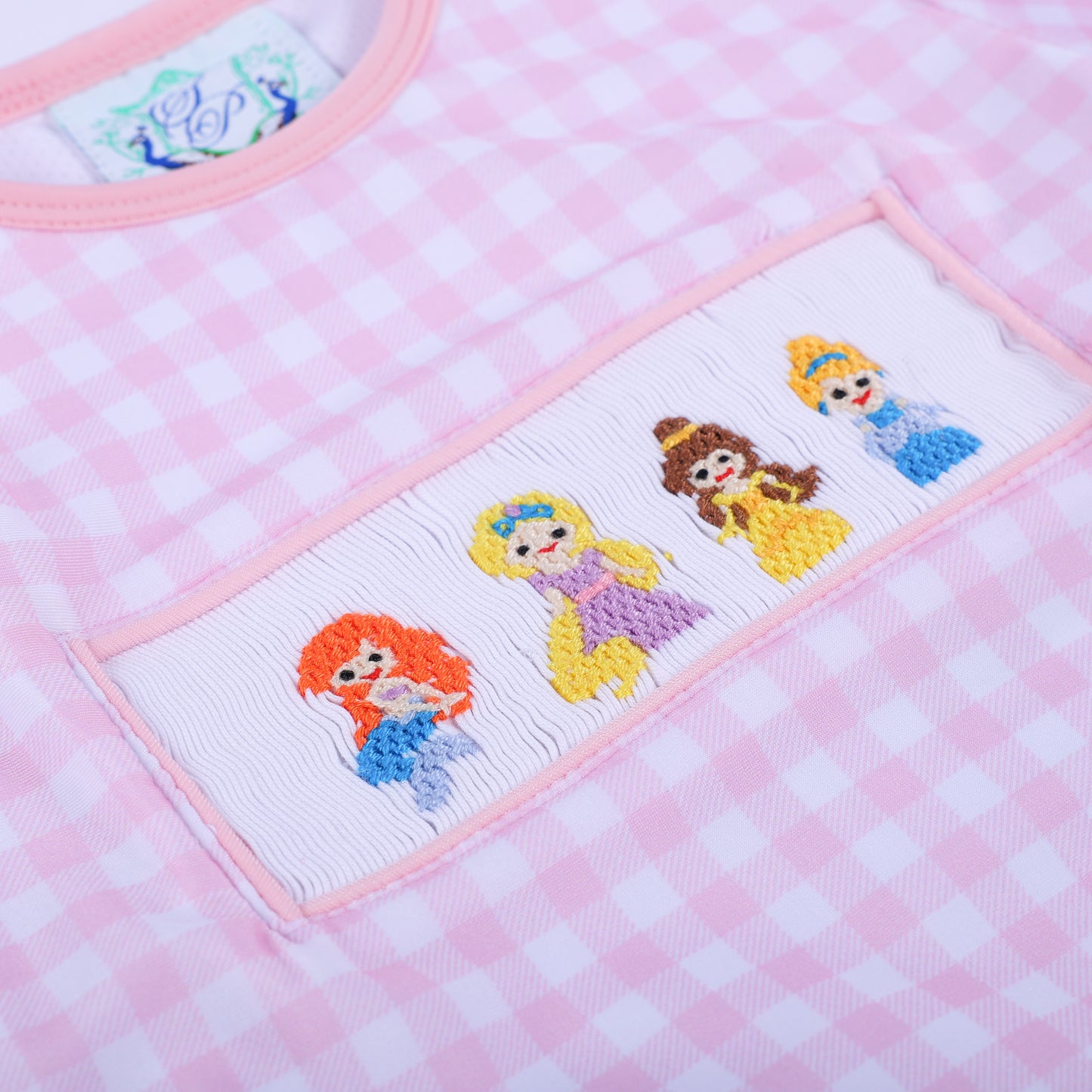 Angled close up view showcasing the detailed hand smocked fairytale princess embroidery on the girls gingham swim top.