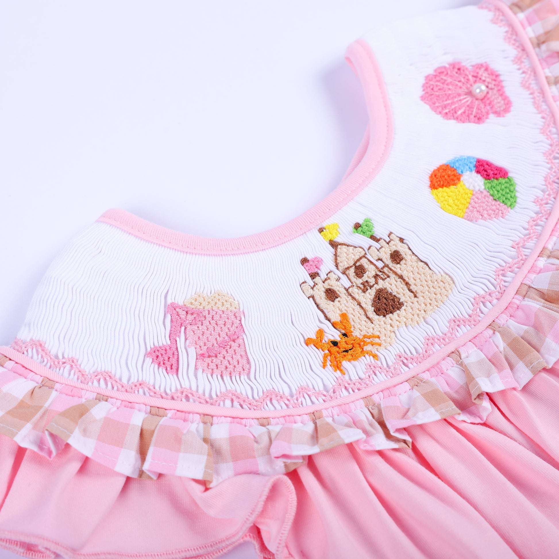 Intricate hand smocked collar featuring hand embroidered sandcastle, orange crab, and bucket motifs for girls.