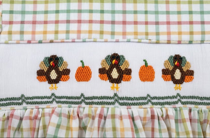 Close-up of embroidered Thanksgiving turkeys and orange pumpkins on a smocked chest panel.
