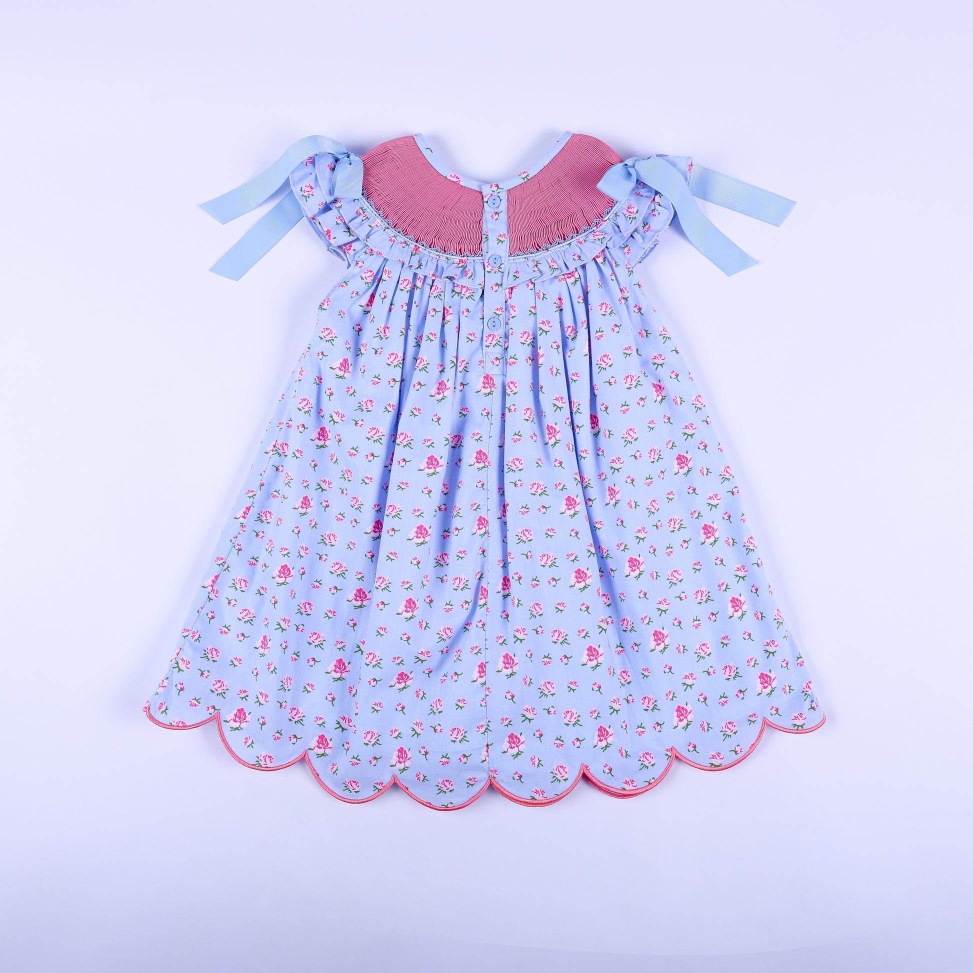 Full back view of girls light blue floral hand-smocked dress featuring back button closure and shoulder ribbons.