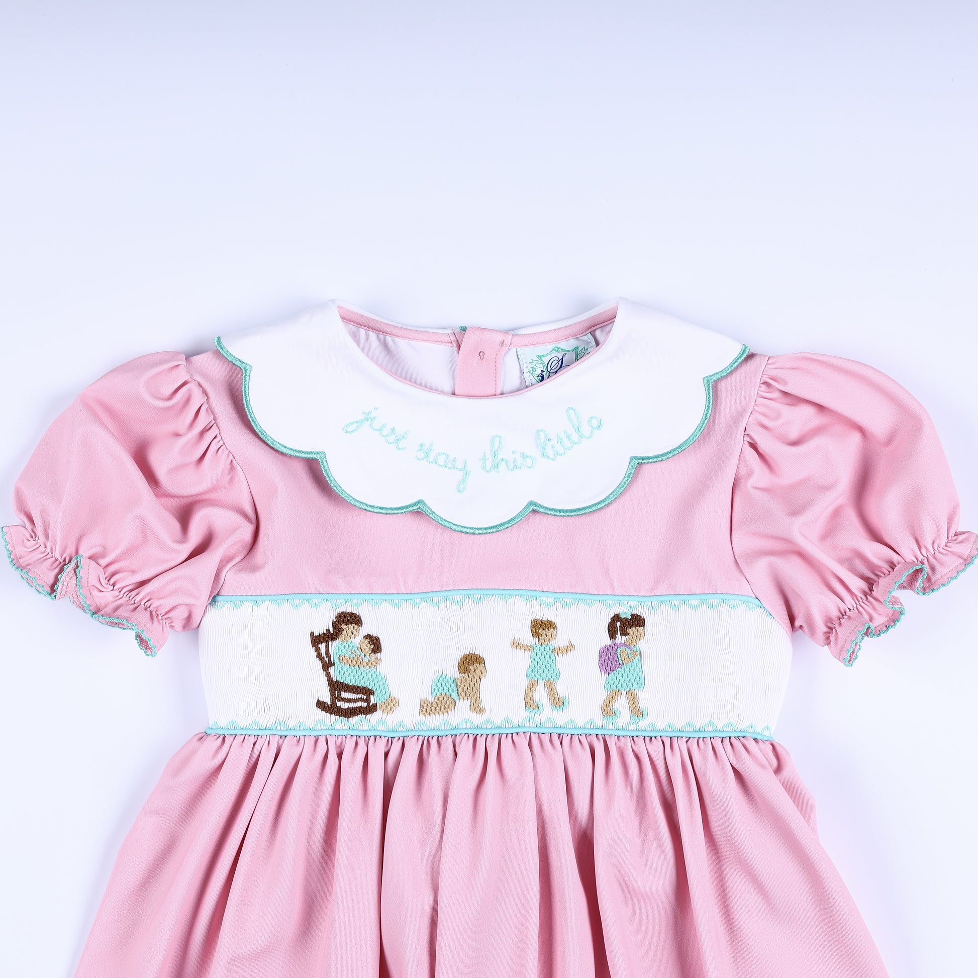 Close-up of hand-smocked pink bodice with growing-up embroidery figures and scalloped Peter Pan collar.