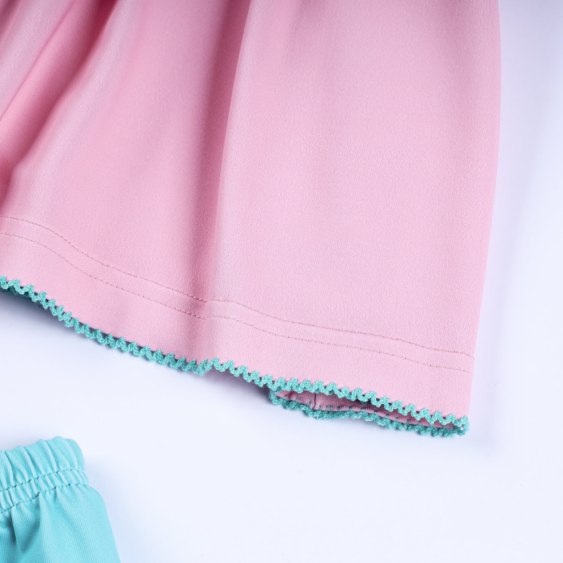 Close-up of baby girl pink dress hemline featuring delicate turquoise embroidered scalloped ric-rac trim.