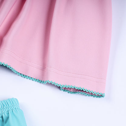 Close-up of baby girl pink dress hemline featuring delicate turquoise embroidered scalloped ric-rac trim.