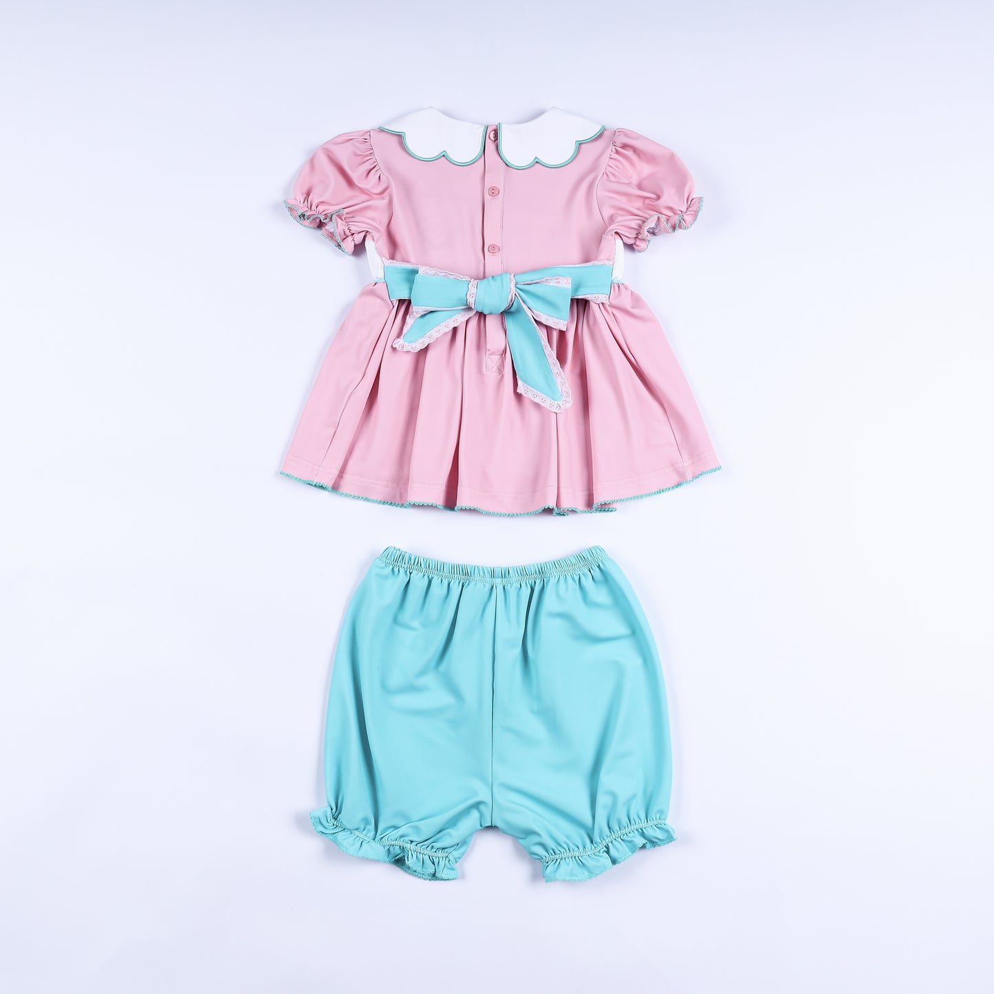Back view of pink hand-smocked dress set showing turquoise sash bow closure and matching ruffle bloomers.