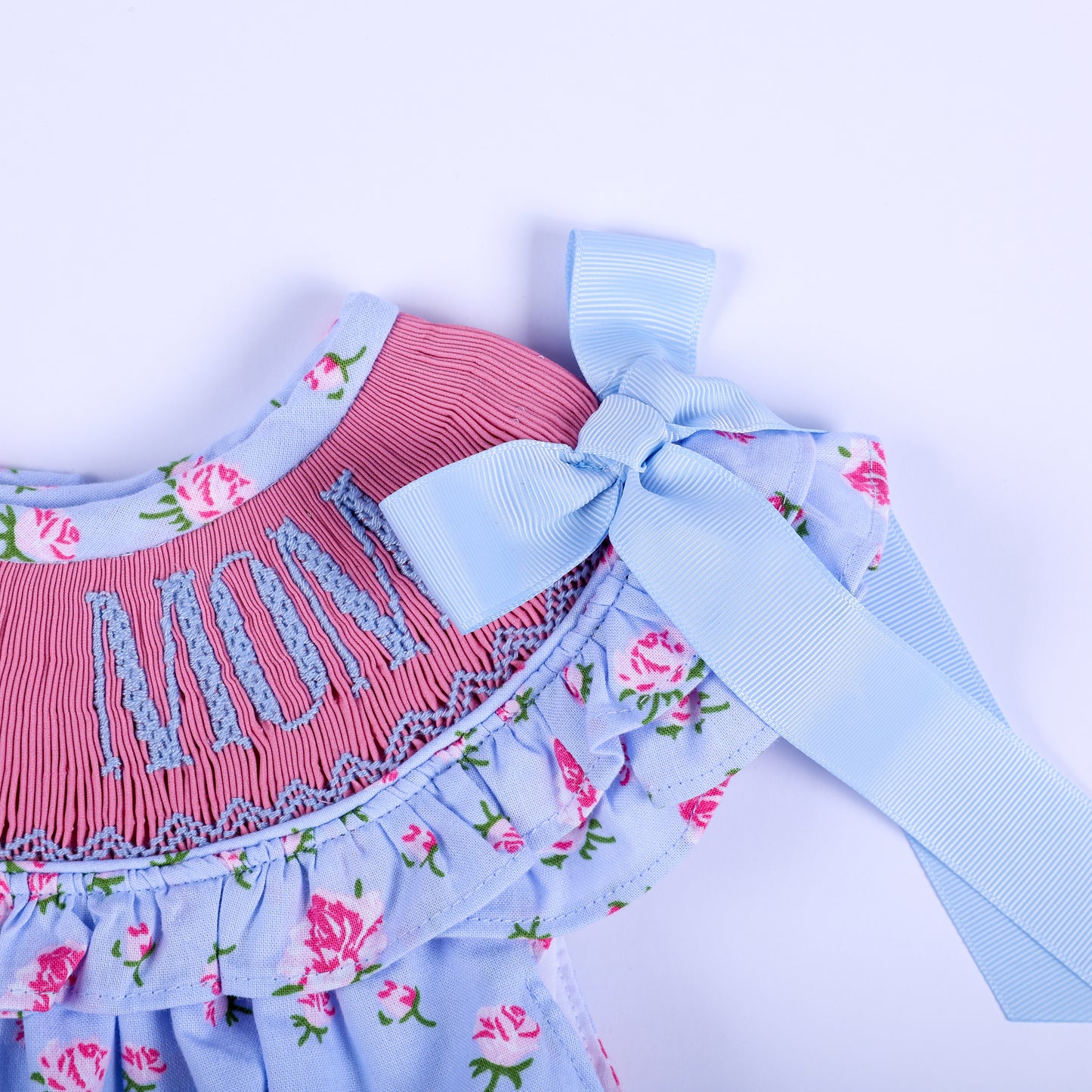 Blue ribbon bow tie strap on ruffle sleeve of I Love Mom floral smocked baby bubble romper detail view.