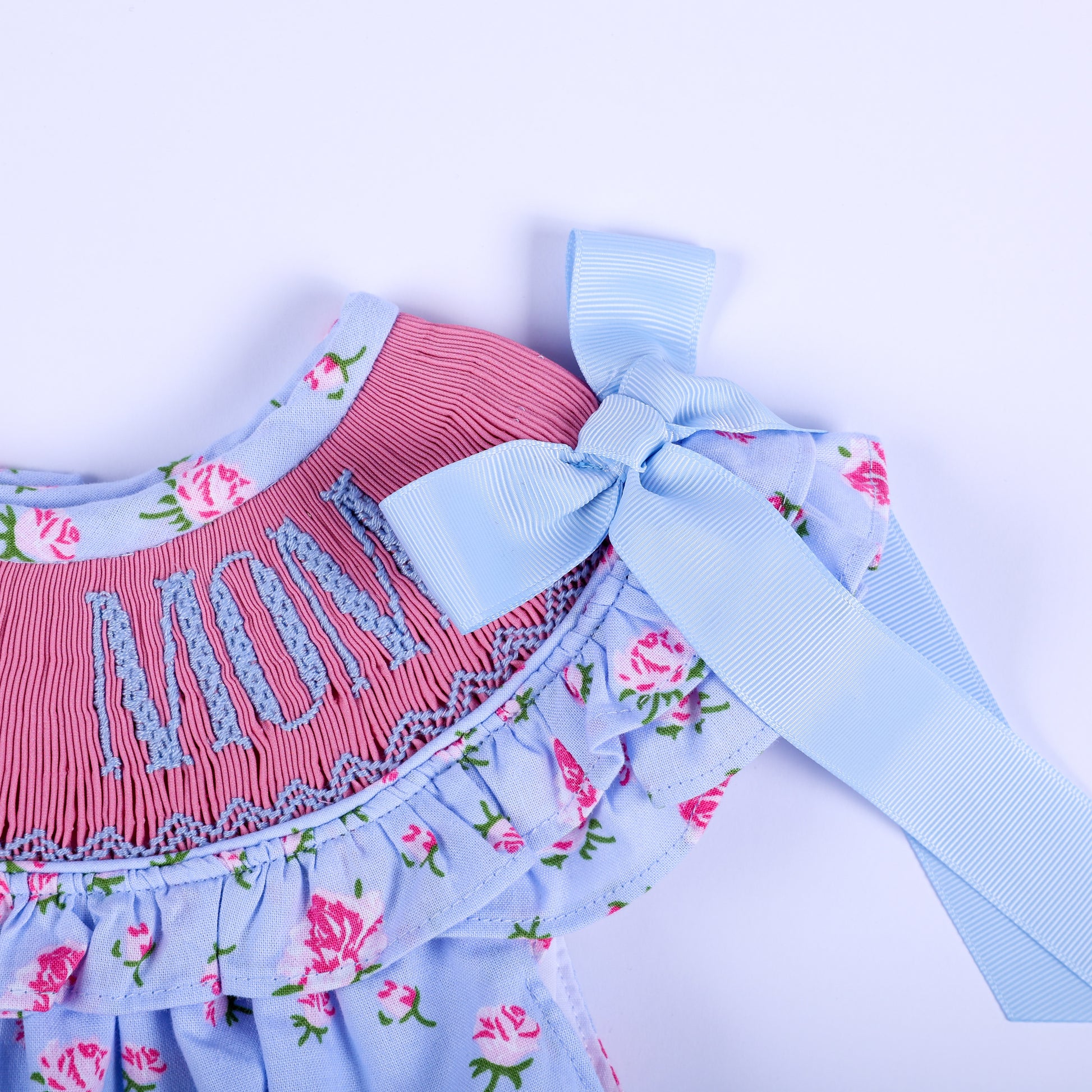 Blue ribbon bow tie strap on ruffle sleeve of I Love Mom floral smocked baby bubble romper detail view.