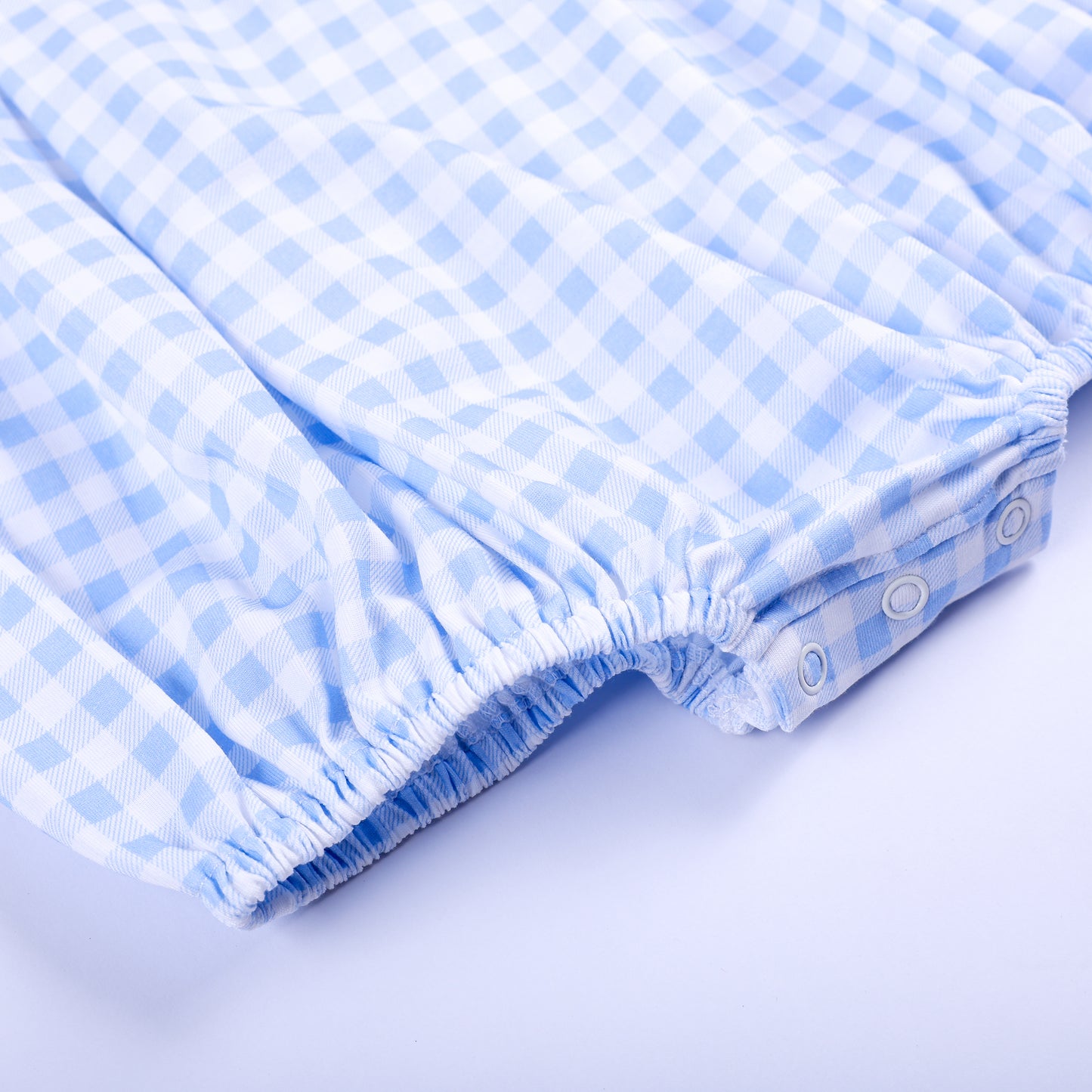 Detailed view of elasticized leg openings with bottom snap closures on blue gingham baby bubble romper.