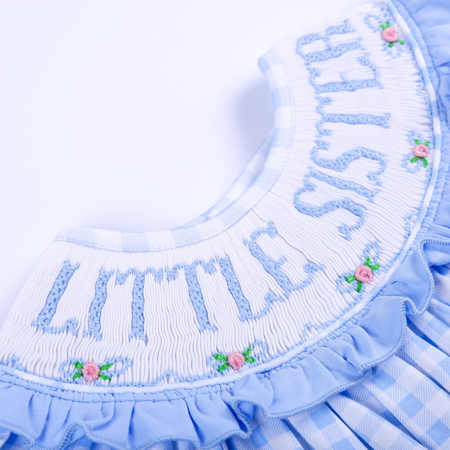 Close-up of intricate hand-smocked white collar with blue Little Sister embroidery and pink floral details.