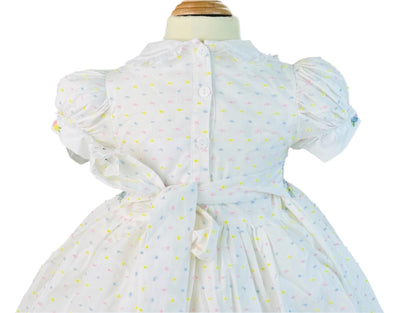 Back view of a white hand-smocked dress with blue flower basket embroidery, buttons, and a large sash bow.