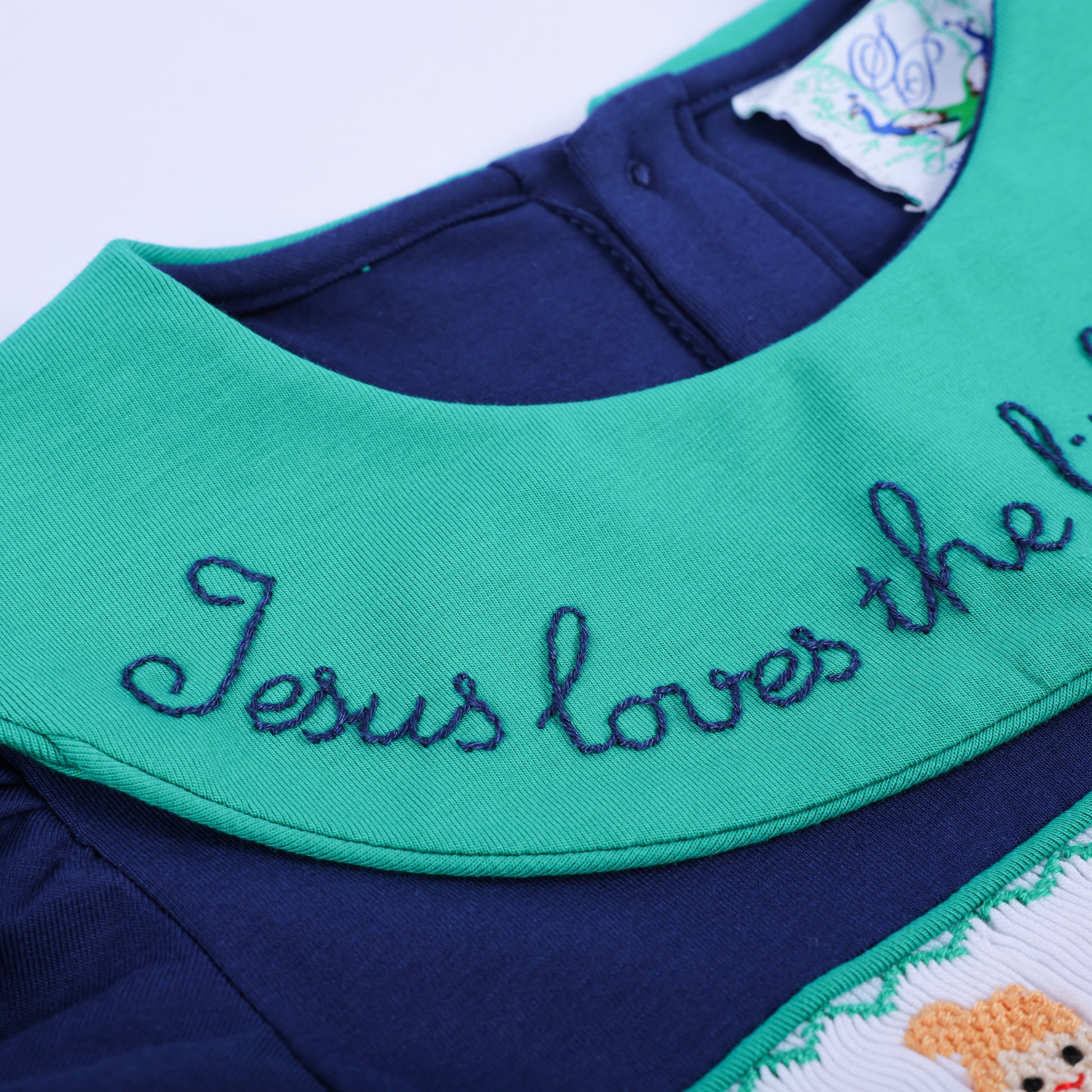 An extreme close-up of the navy smocked dress, highlighting the vibrant green hand-embroidered collar text detail.