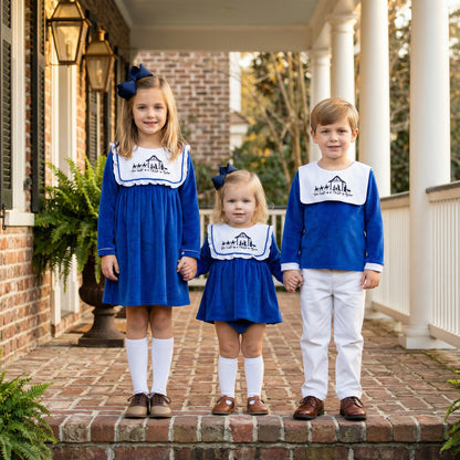Three siblings in matching blue velvet Christmas outfits with white bib collars featuring embroidered Nativity scene.