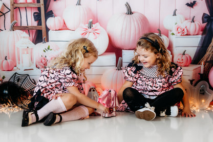 Two toddler girls playing in matching Batty for Bows hand smocked pink dresses with black embroidered bat pattern.