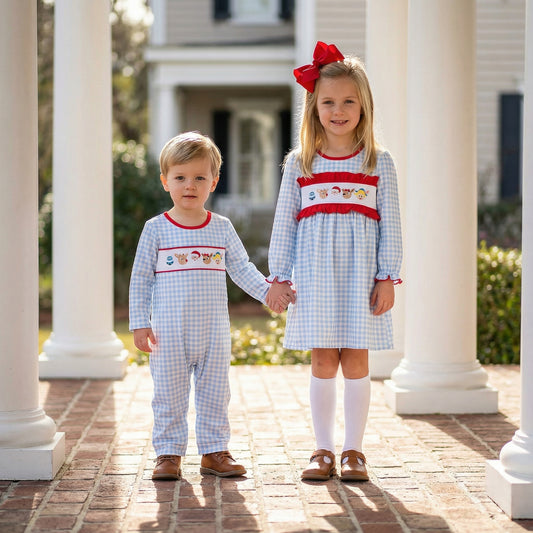 Siblings holding hands on porch in matching blue gingham smocked Christmas outfits with Rudolph, elf, and snowman.