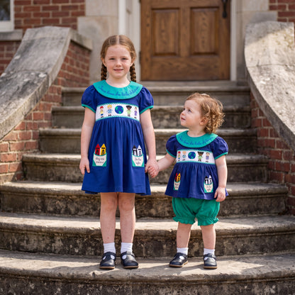Two sisters holding hands in matching blue smocked outfits, including a toddler bloomer set and a girls dress