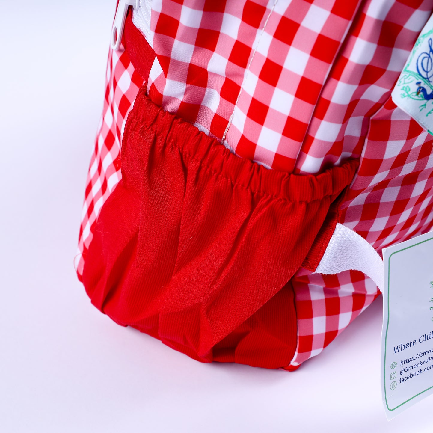 Side view showing elastic side pocket on boys hand-smocked Mickey Mouse red gingham full-size backpack.