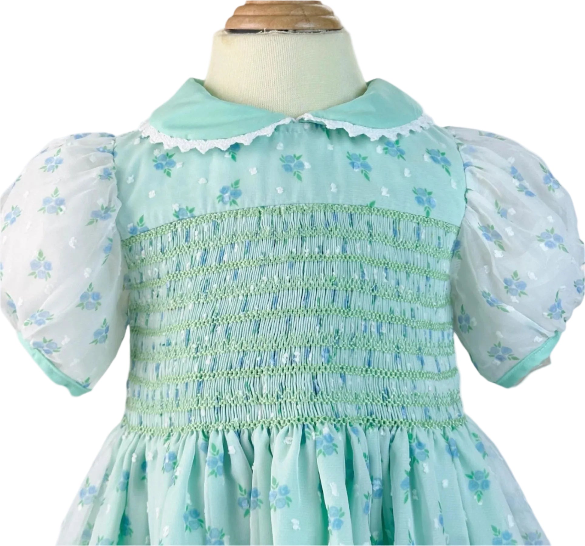 Hand smocked children's dress in mint chiffon with blue roses and white Swiss dots, featuring puff sleeves and a lace-trimmed collar.