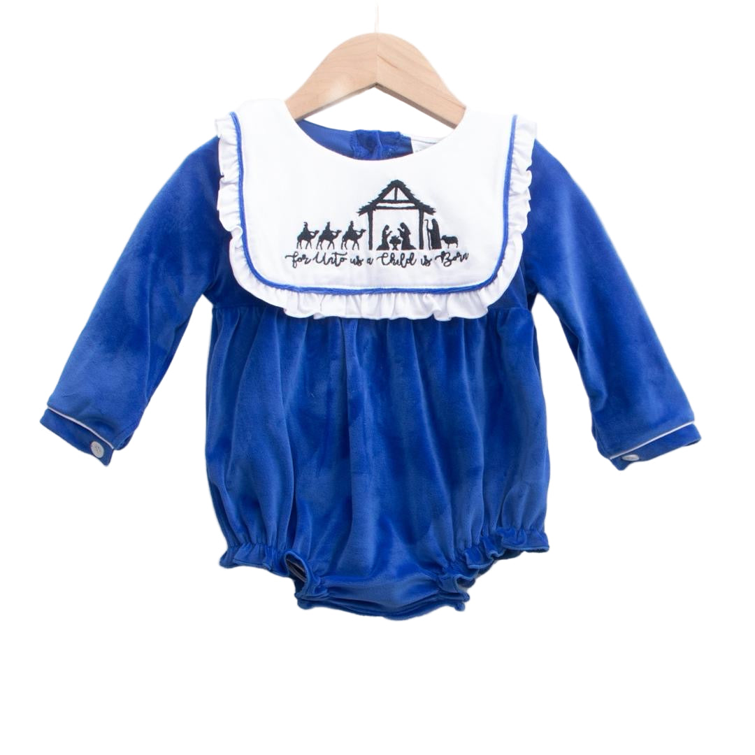 Blue velvet girl bubble with white smocked collar embroidered with a Christmas Nativity scene and "For Unto Us a Child is Born" text.