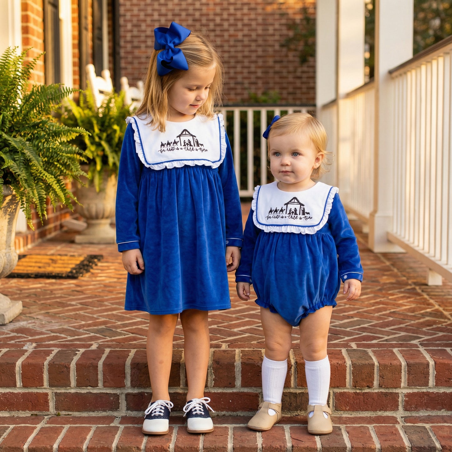 Sisters matching in royal blue velour dress and bubble with embroidered nativity bib collars.