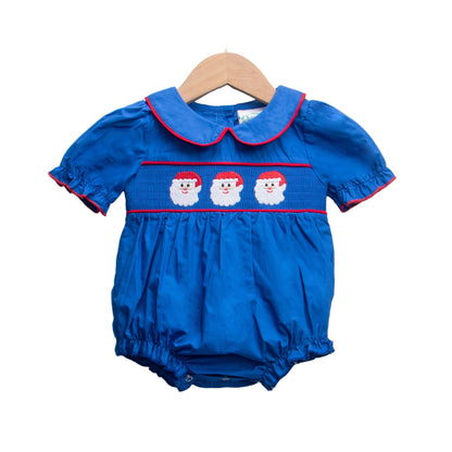 Girls navy blue smocked Christmas bubble romper with three embroidered Santa faces, puff sleeves, and red trim.