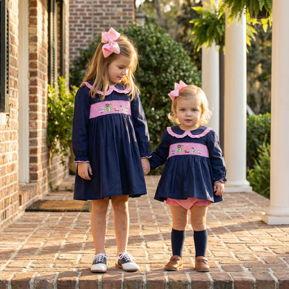 Sisters holding hands wearing matching navy and pink smocked nativity dress and ruffle diaper set.
