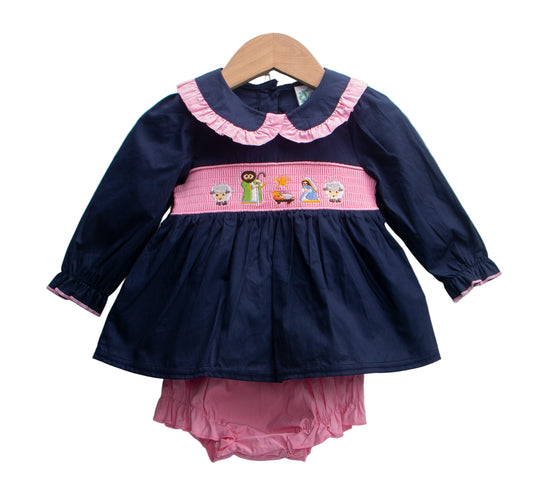 Navy woven cotton diaper set featuring pink smocked nativity scene, ruffle collar, and matching bloomers.