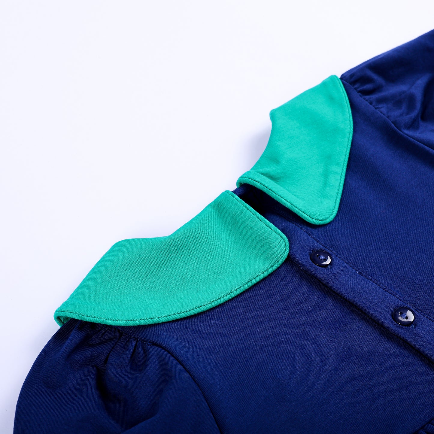 Close-up view of back button placket closure and green Peter Pan collar on navy smocked toddler top.