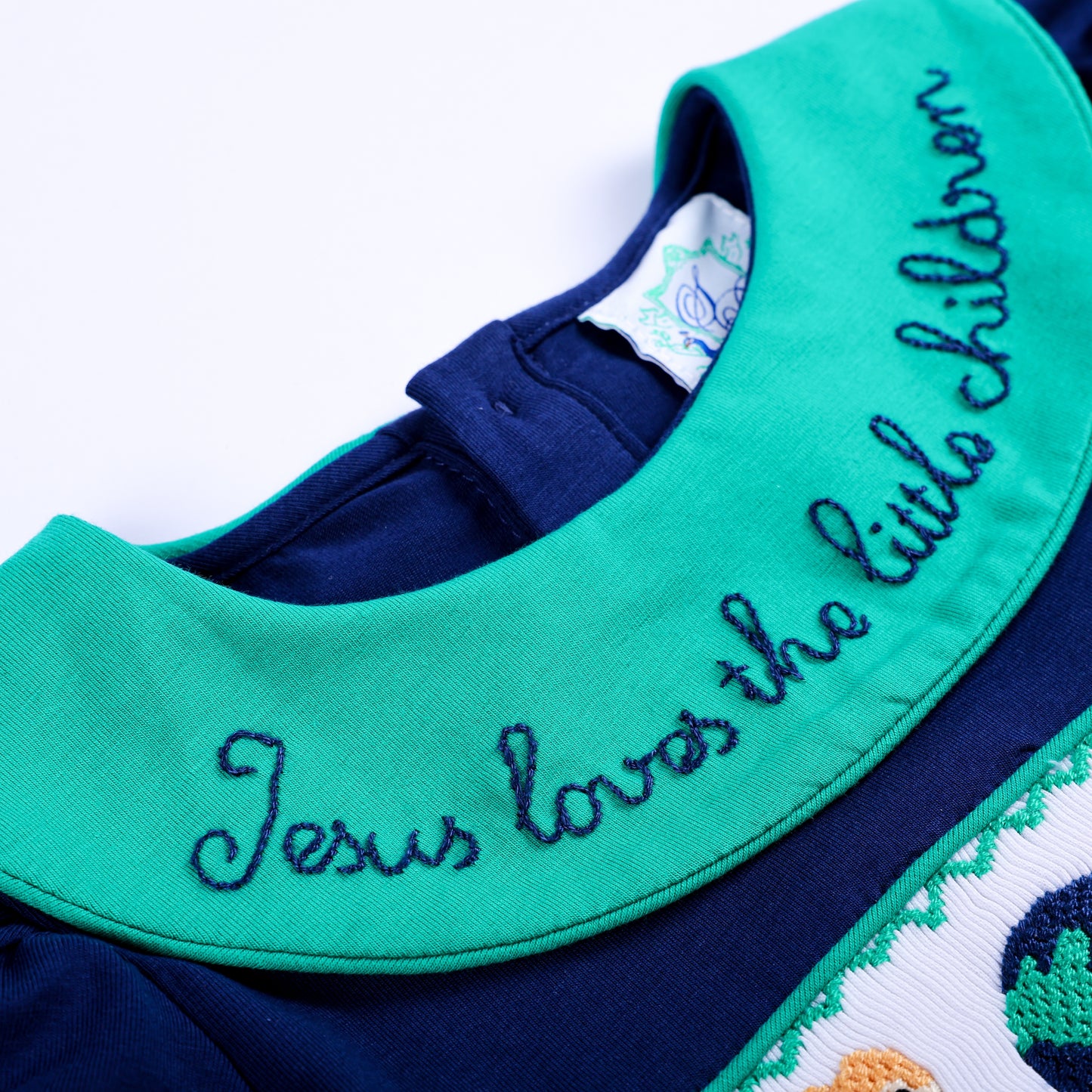 Detailed close-up of green Peter Pan collar with embroidered navy script reading Jesus loves the little children.