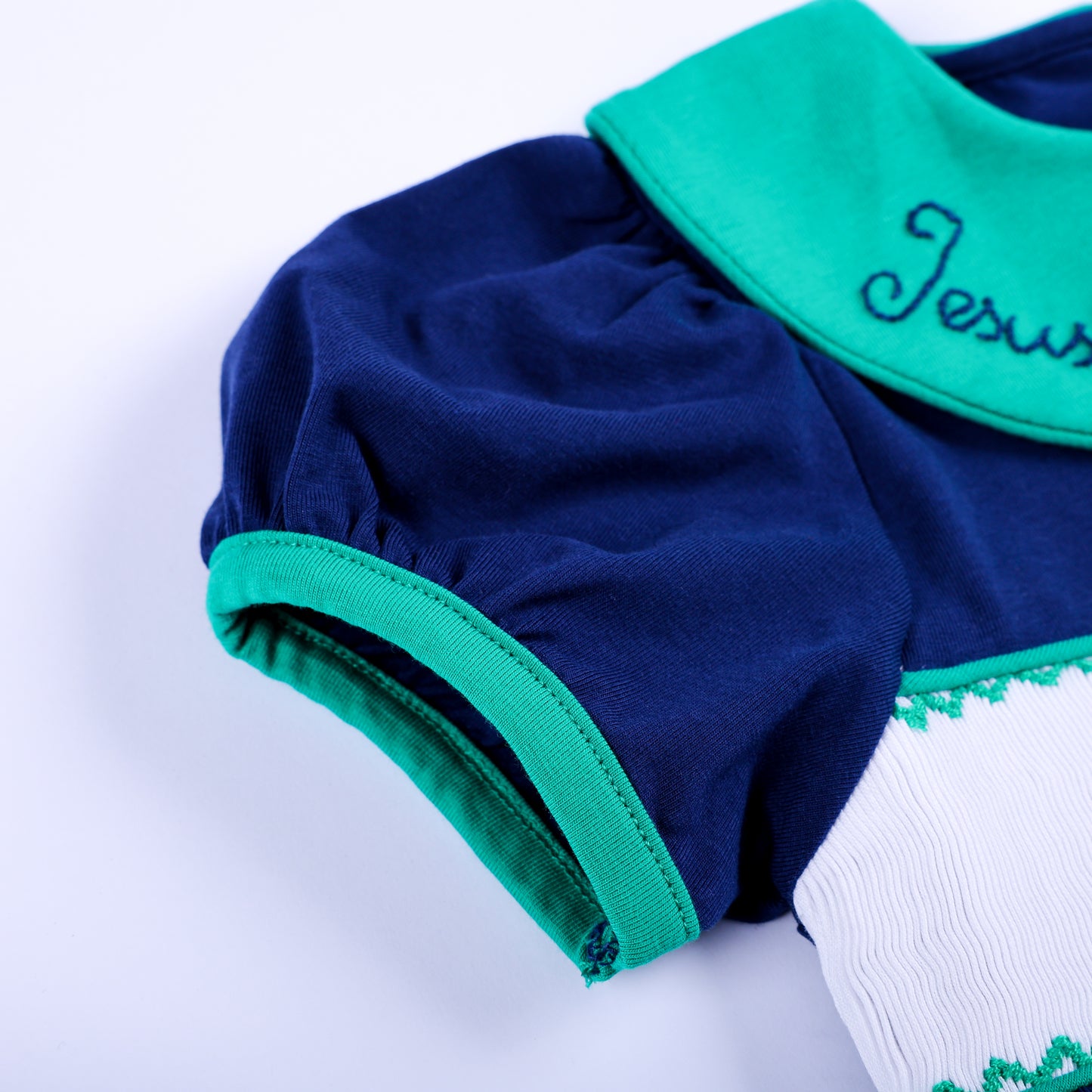 Close-up shot of navy short puff sleeve with green bias trim piping on hand smocked toddler clothing set.