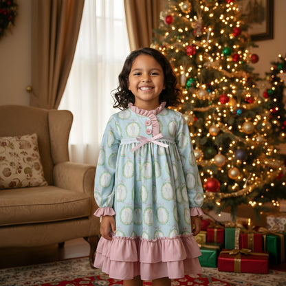 Young girl smiling in Nutcracker Ballet aqua blue and pink holiday nightgown by a festive Christmas tree.