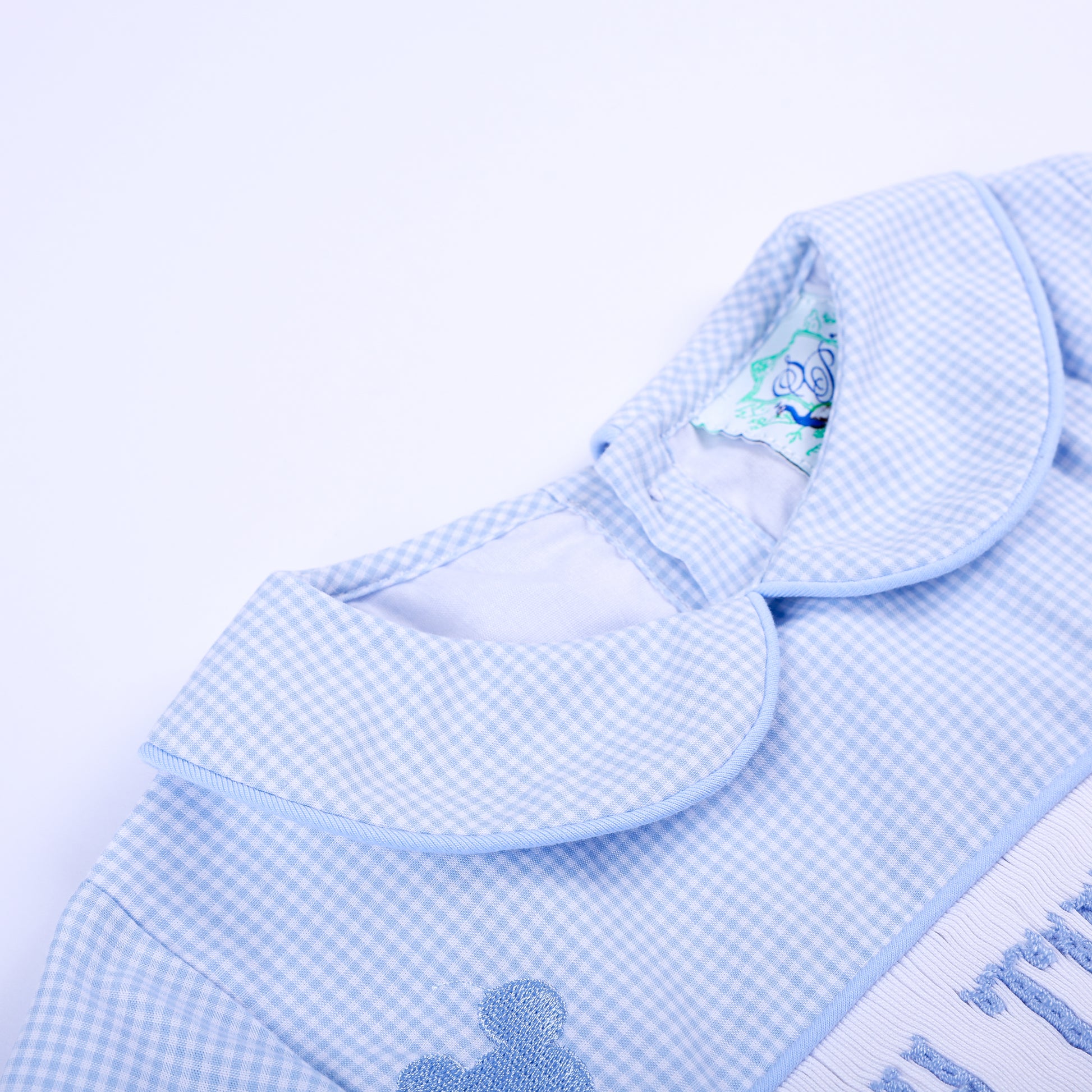Close-up shot of neat Peter Pan collar and soft inner neck lining of Oh Twodles hand smocked blue gingham boys bubble.