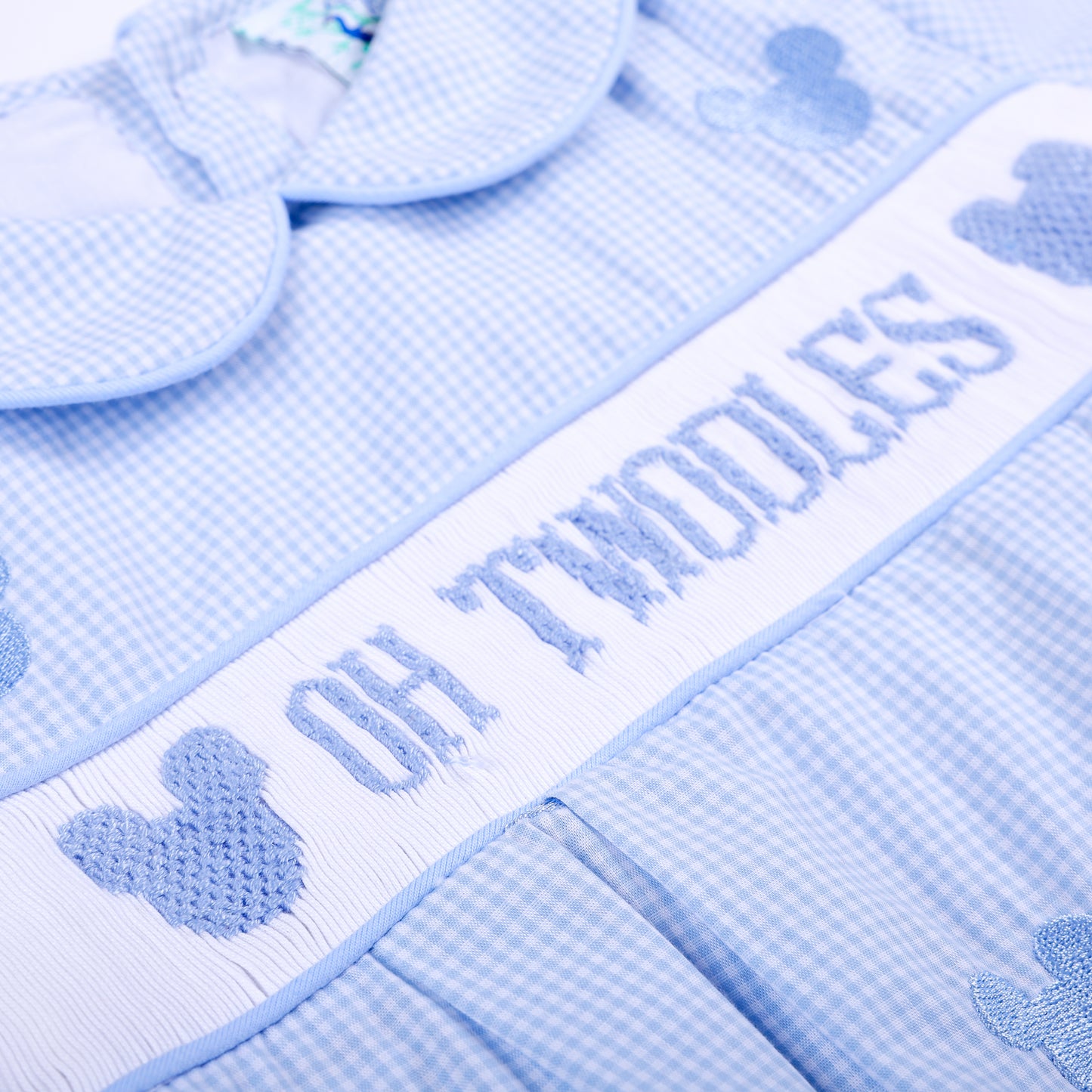 Angled close-up of hand smocked Oh Twodles lettering and blue embroidered mouse silhouette on vintage boys bubble.