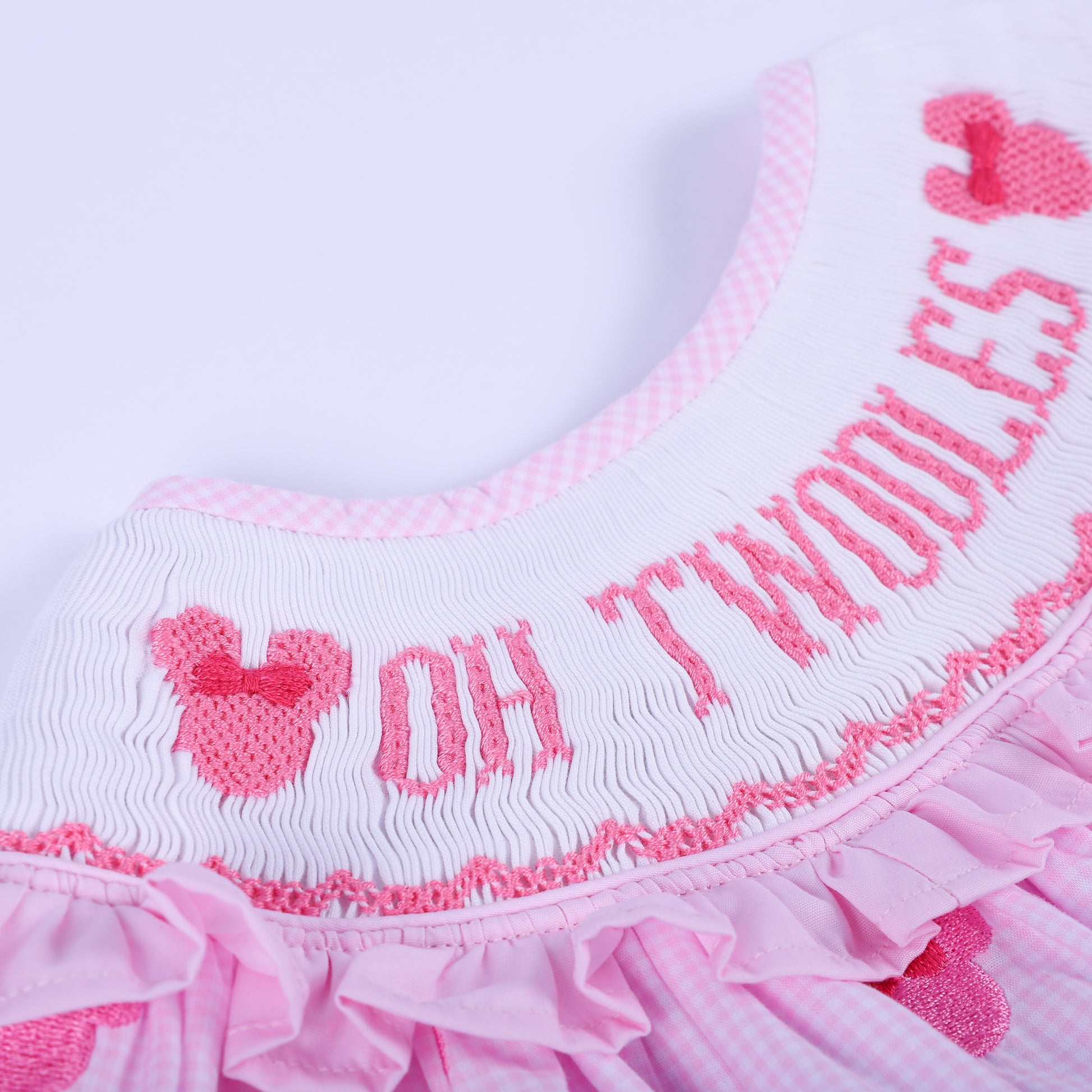 Macro detail of Oh Twoodles hand embroidered text on smocked ruffled neck collar of pink gingham baby outfit.